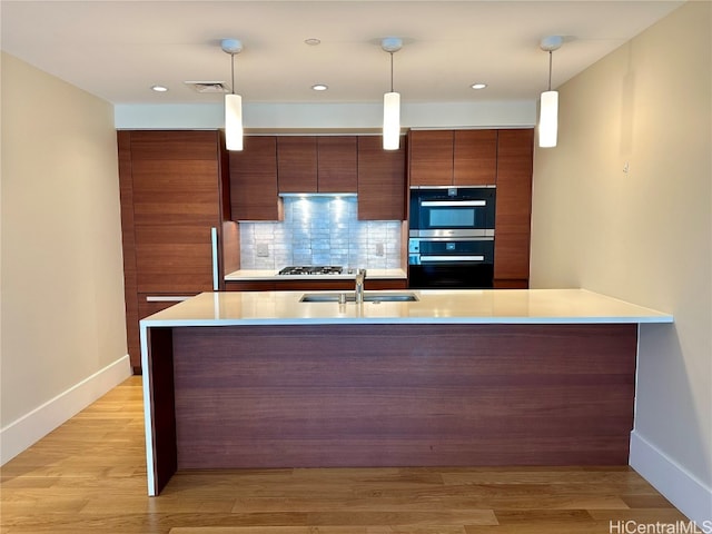 kitchen featuring decorative backsplash, sink, light hardwood / wood-style floors, decorative light fixtures, and stainless steel double oven