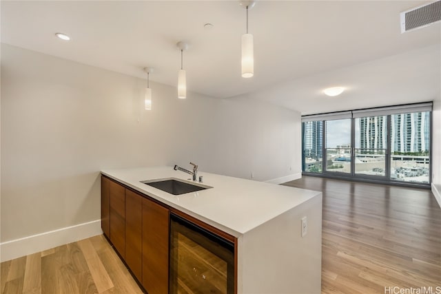 kitchen featuring light hardwood / wood-style flooring, wine cooler, sink, decorative light fixtures, and a wall of windows