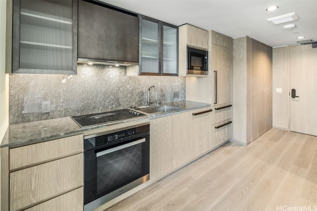 kitchen featuring appliances with stainless steel finishes, sink, light hardwood / wood-style floors, dark stone counters, and decorative backsplash