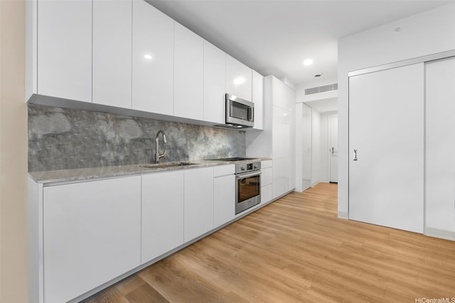 987 Queen St Unit 508, Honolulu, HI 96814 - kitchen with appliances with stainless steel finishes, white cabinetry, light wood-style flooring, backsplash, and light stone counters
