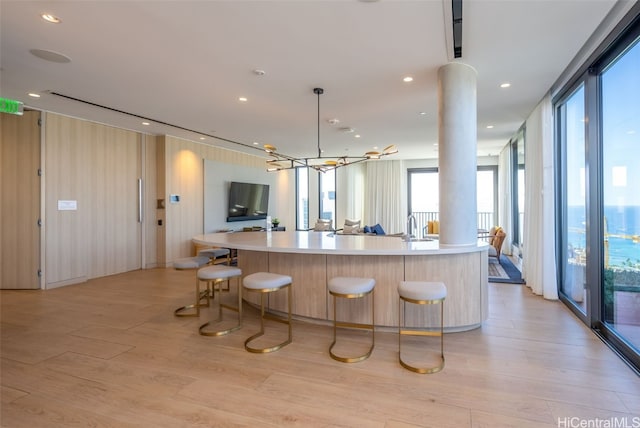 kitchen featuring sink, a breakfast bar, a notable chandelier, pendant lighting, and light wood-type flooring