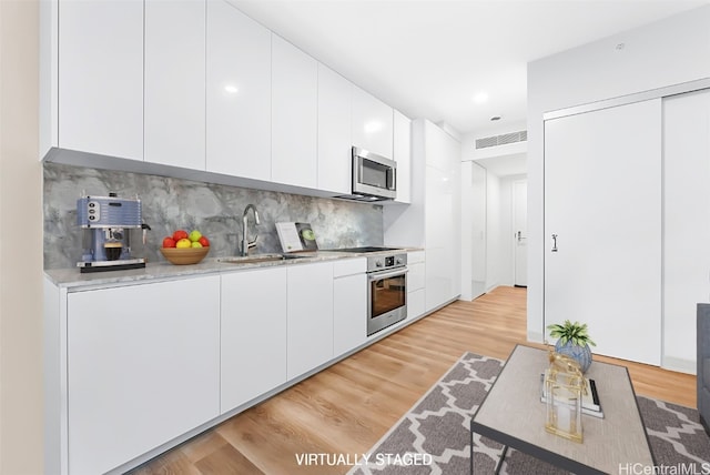 kitchen with stainless steel appliances, sink, light wood-type flooring, white cabinets, and tasteful backsplash