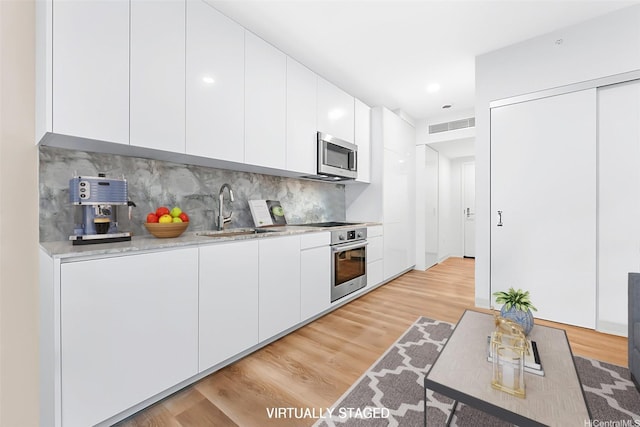 987 Queen St Unit 508, Honolulu, HI 96814 - kitchen with stainless steel appliances, white cabinets, light wood-style floors, backsplash, and light countertops