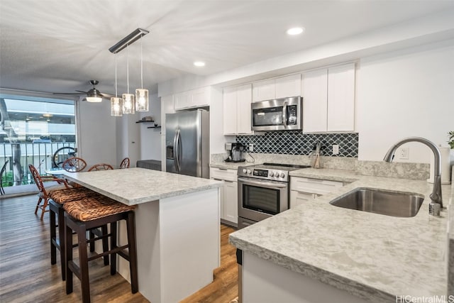 kitchen with sink, a kitchen breakfast bar, white cabinetry, stainless steel appliances, and decorative light fixtures