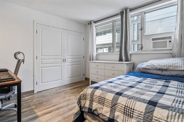 bedroom featuring light hardwood / wood-style floors, cooling unit, a textured ceiling, and a closet