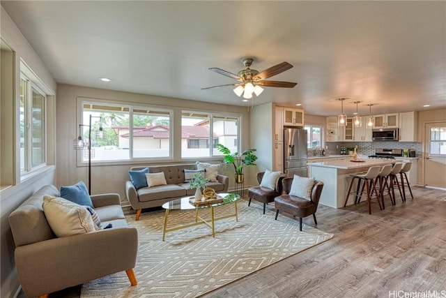 living room featuring ceiling fan, plenty of natural light, sink, and light wood-type flooring