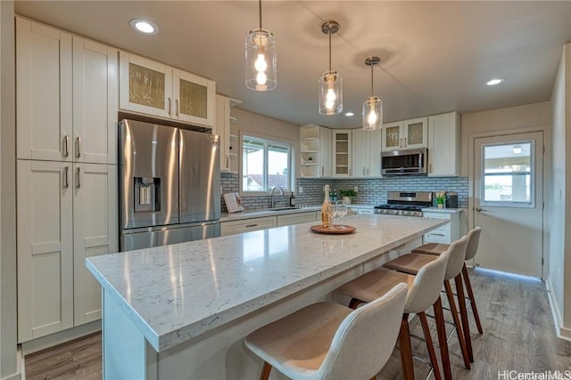 kitchen featuring pendant lighting, appliances with stainless steel finishes, white cabinetry, light stone countertops, and a kitchen island