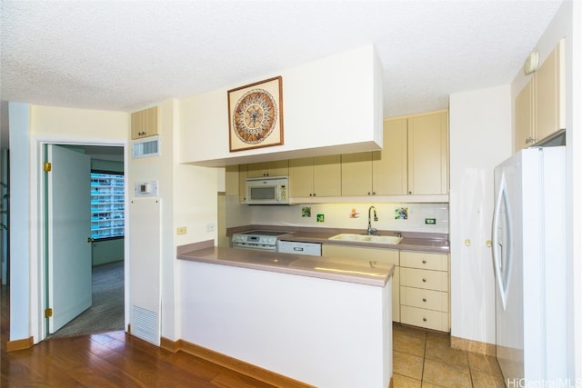 kitchen with kitchen peninsula, white appliances, sink, and a textured ceiling