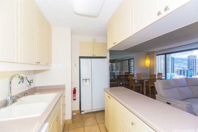 kitchen featuring white fridge with ice dispenser, a textured ceiling, sink, backsplash, and light tile patterned flooring