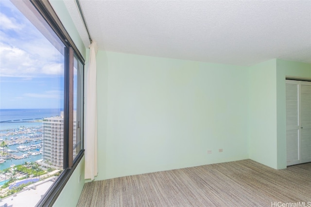 carpeted spare room with a water view and a textured ceiling