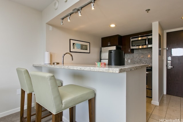 kitchen featuring tasteful backsplash, kitchen peninsula, stainless steel appliances, dark brown cabinetry, and a breakfast bar area