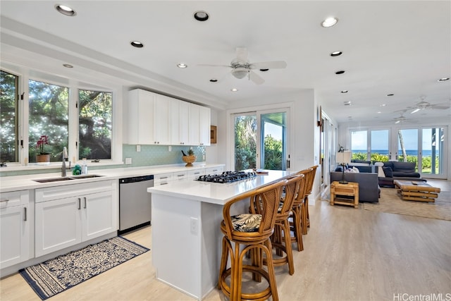 kitchen with a kitchen island, stainless steel appliances, sink, white cabinetry, and light hardwood / wood-style floors