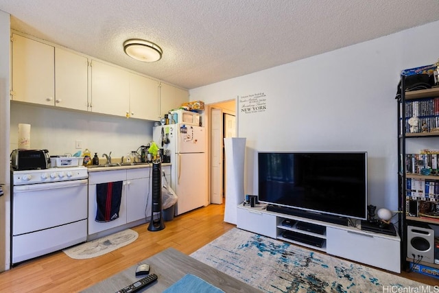 kitchen with white appliances, white cabinets, sink, a textured ceiling, and light hardwood / wood-style floors