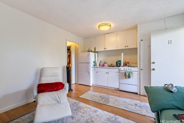 kitchen with white cabinets, light hardwood / wood-style floors, white appliances, and a textured ceiling