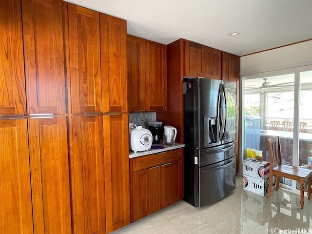 kitchen featuring ceiling fan, backsplash, light stone countertops, and stainless steel fridge