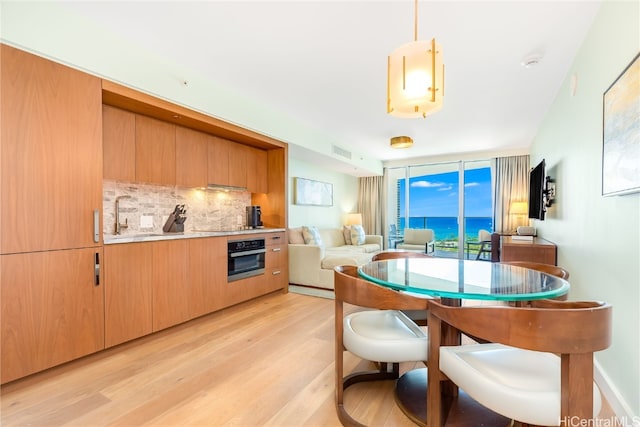 kitchen with sink, backsplash, stainless steel oven, light hardwood / wood-style floors, and pendant lighting