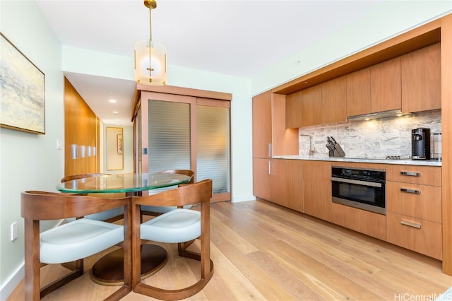 kitchen featuring decorative backsplash, oven, exhaust hood, pendant lighting, and light wood-type flooring