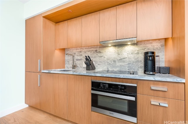 kitchen with oven, sink, black electric cooktop, light hardwood / wood-style floors, and decorative backsplash