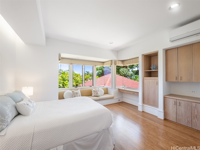 bedroom with a wall mounted air conditioner, multiple windows, and light hardwood / wood-style floors