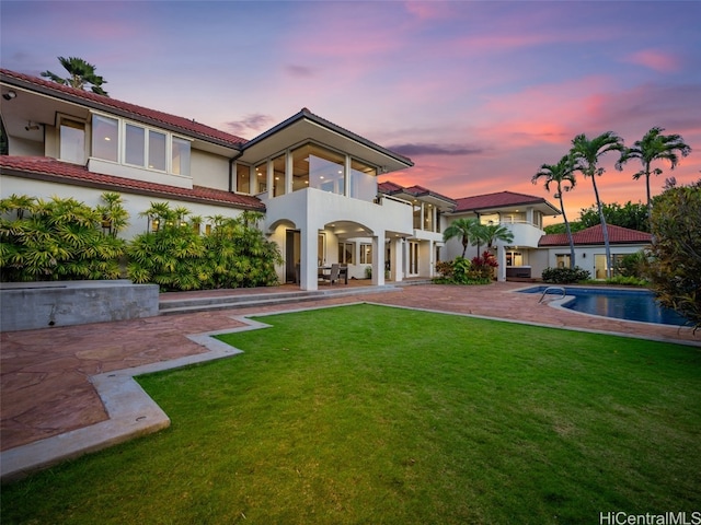 back house at dusk featuring a patio, a balcony, and a yard