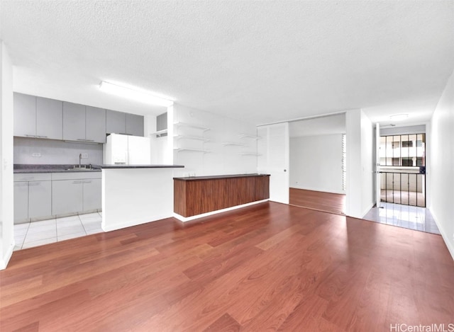 kitchen with white refrigerator with ice dispenser, a sink, gray cabinets, light wood finished floors, and dark countertops