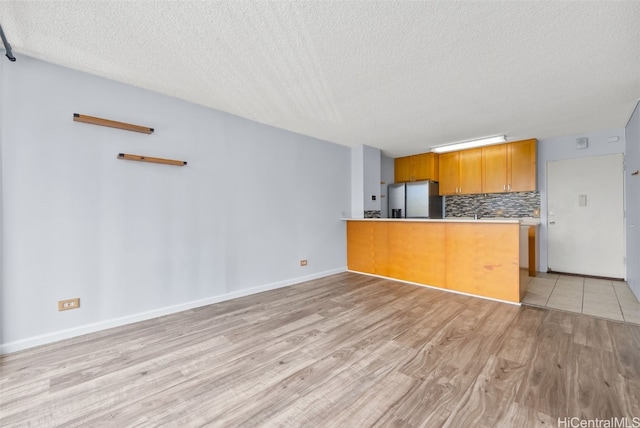 kitchen featuring stainless steel refrigerator with ice dispenser, kitchen peninsula, light hardwood / wood-style flooring, and a textured ceiling