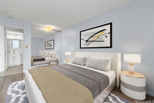 bedroom featuring ensuite bath, wood-type flooring, and a textured ceiling