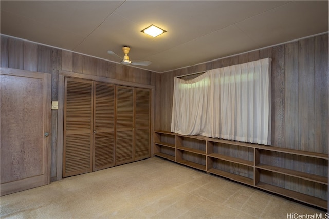 interior space with a closet, ceiling fan, wood walls, and carpet flooring