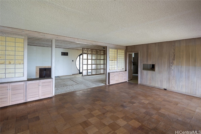 empty room with wooden walls, a brick fireplace, a textured ceiling, and plenty of natural light