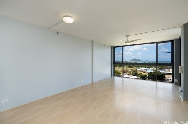 empty room featuring a wall of windows, light wood-type flooring, and ceiling fan