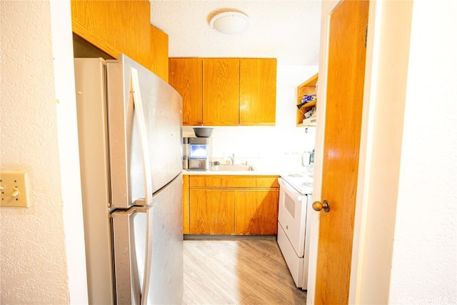 kitchen featuring white appliances, a textured ceiling, light hardwood / wood-style flooring, and sink