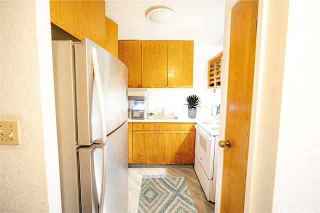 kitchen with light hardwood / wood-style floors, a textured ceiling, sink, and white appliances