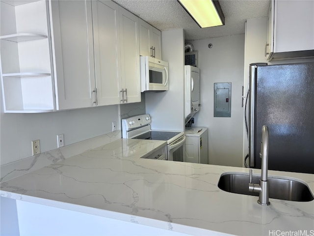 kitchen featuring white appliances, light stone countertops, a textured ceiling, white cabinetry, and stacked washing maching and dryer