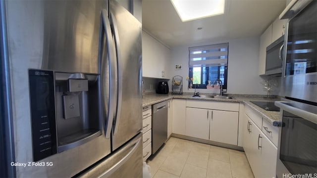 kitchen featuring sink, light stone countertops, white cabinets, light tile patterned floors, and appliances with stainless steel finishes