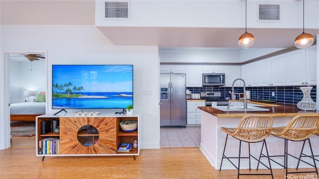 kitchen featuring kitchen peninsula, a breakfast bar, stainless steel appliances, pendant lighting, and white cabinets