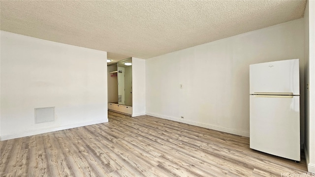 empty room with a textured ceiling and light hardwood / wood-style flooring