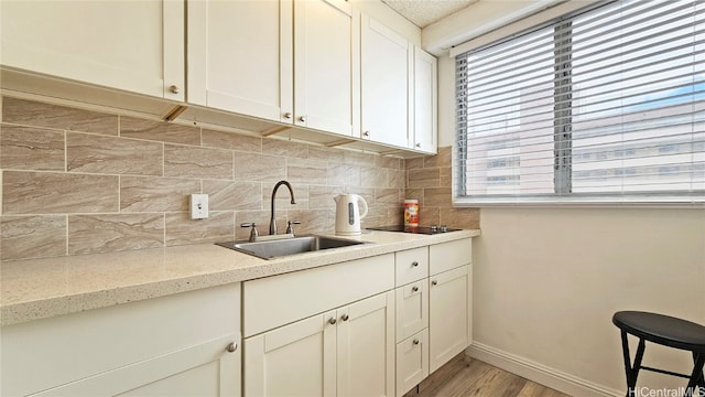 kitchen featuring sink, light wood-type flooring, backsplash, black electric cooktop, and light stone counters