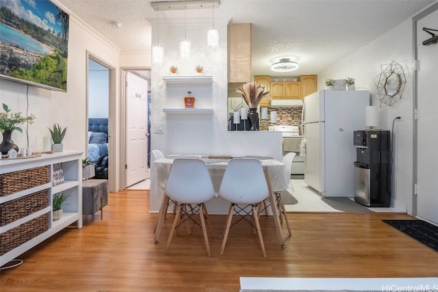 kitchen with white appliances, a textured ceiling, hanging light fixtures, light hardwood / wood-style floors, and light brown cabinets