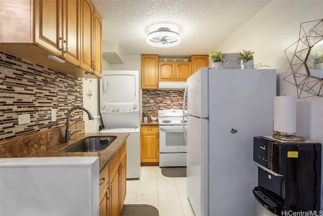 kitchen featuring tasteful backsplash, a textured ceiling, stacked washer and dryer, sink, and white appliances