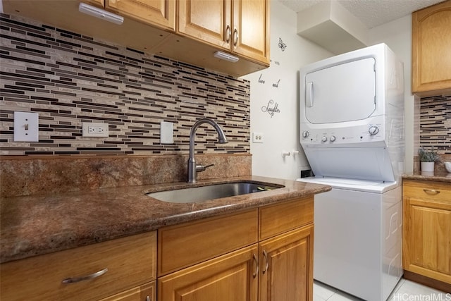 laundry room featuring cabinets, light tile patterned floors, a textured ceiling, stacked washer and dryer, and sink