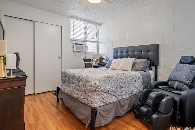 bedroom featuring light hardwood / wood-style floors, a closet, a textured ceiling, and cooling unit