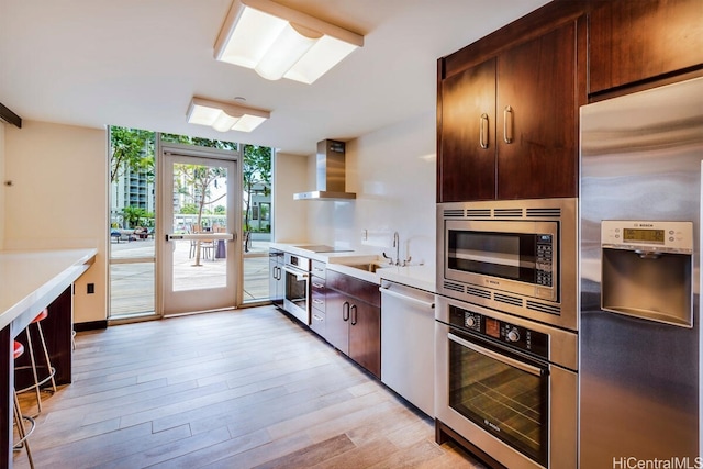 kitchen with wall chimney exhaust hood, sink, light hardwood / wood-style flooring, and stainless steel appliances