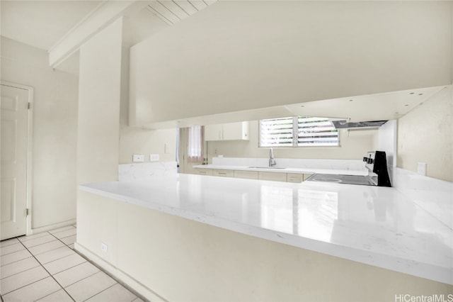 kitchen with black stove, white cabinetry, light tile patterned floors, and kitchen peninsula