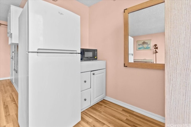 kitchen featuring white cabinetry, white fridge, a textured ceiling, and light wood-type flooring