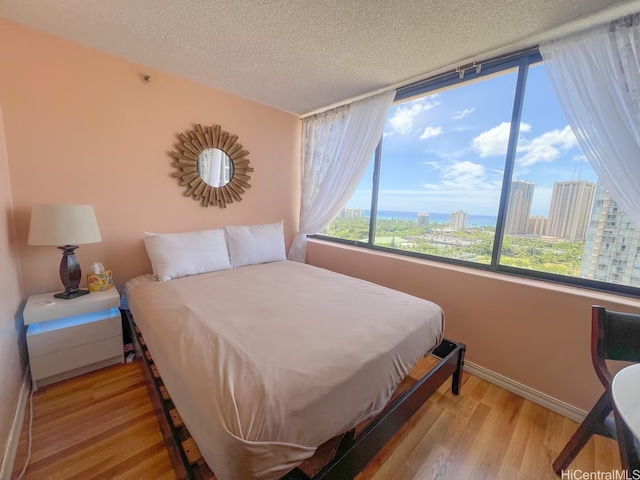 bedroom featuring a view of city, light wood-type flooring, baseboards, and a textured ceiling