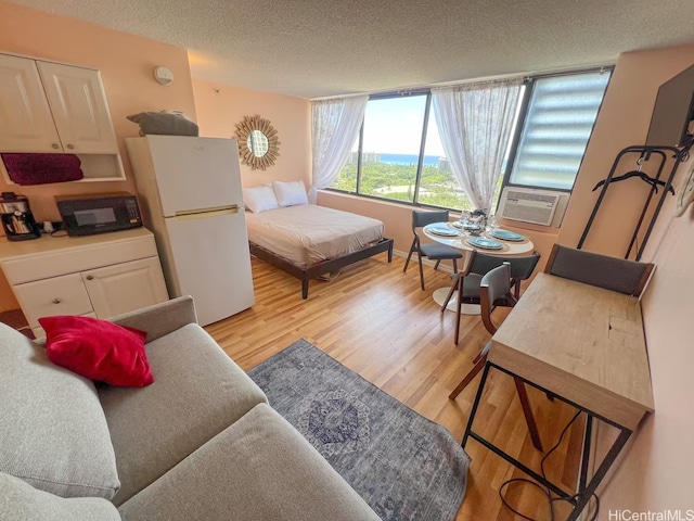 interior space featuring cooling unit, light wood-type flooring, freestanding refrigerator, and a textured ceiling