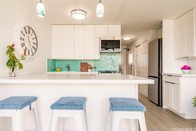 kitchen with white cabinetry, light countertops, a breakfast bar area, and freestanding refrigerator