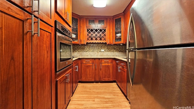 kitchen featuring light stone counters, stainless steel appliances, light wood-type flooring, and tasteful backsplash