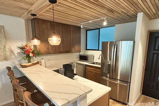 kitchen featuring kitchen peninsula, stainless steel appliances, a breakfast bar, light stone countertops, and decorative light fixtures