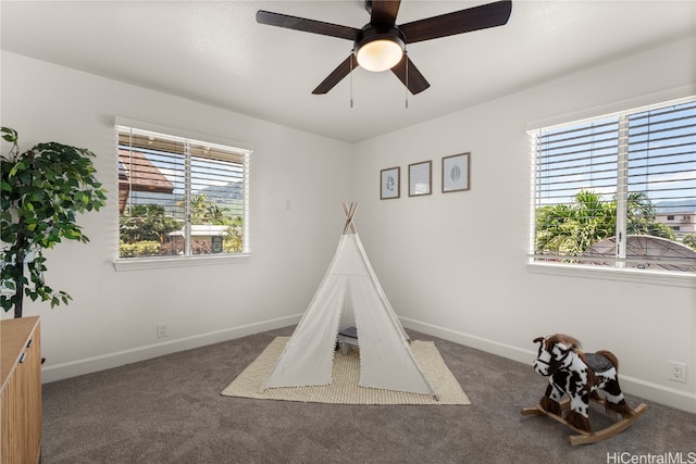 game room with ceiling fan and dark colored carpet